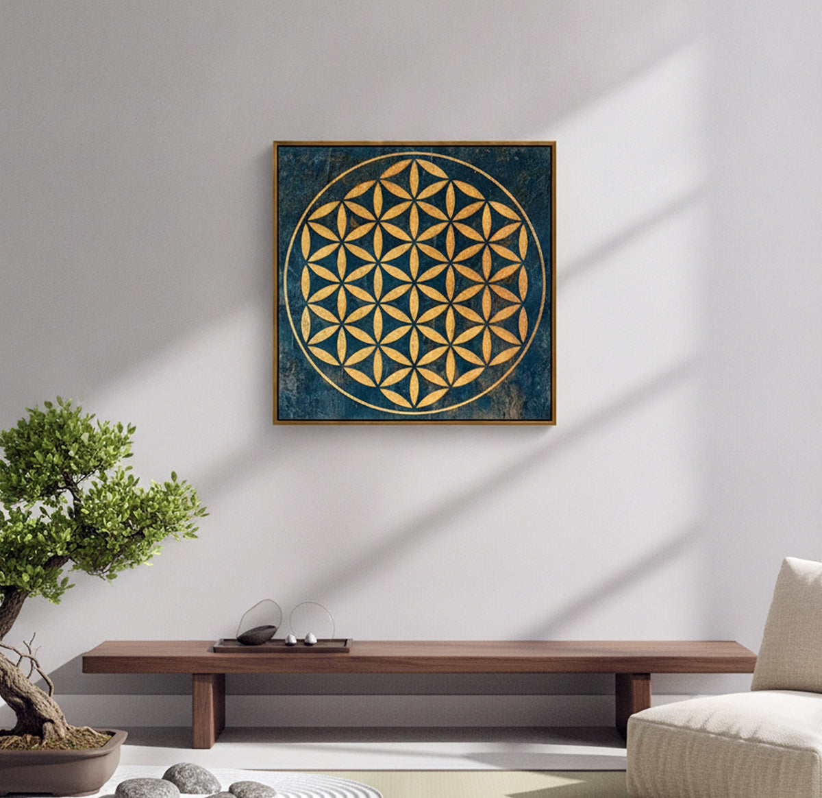 A square framed wall art print featuring a gold Flower of Life geometric design on a textured dark blue background, displayed on a light gray wall in a styled room setting with a wooden bench, bonsai tree, and sofa.
