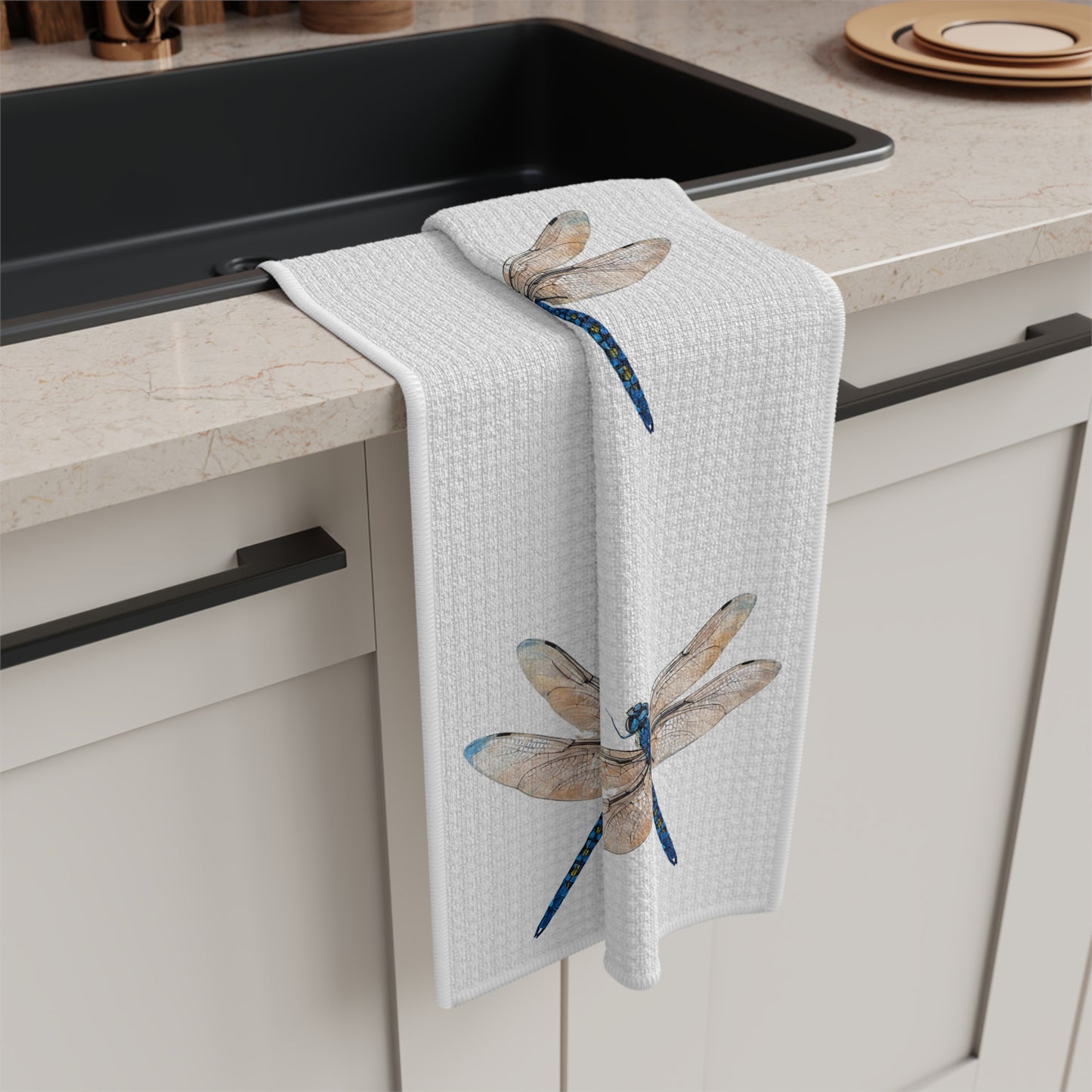 Kitchen towel with dragonfly design hanging on a kitchen cabinet.