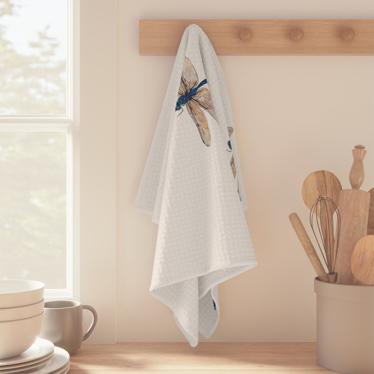 White towel with dragonfly design hanging on a wooden rack in a kitchen.