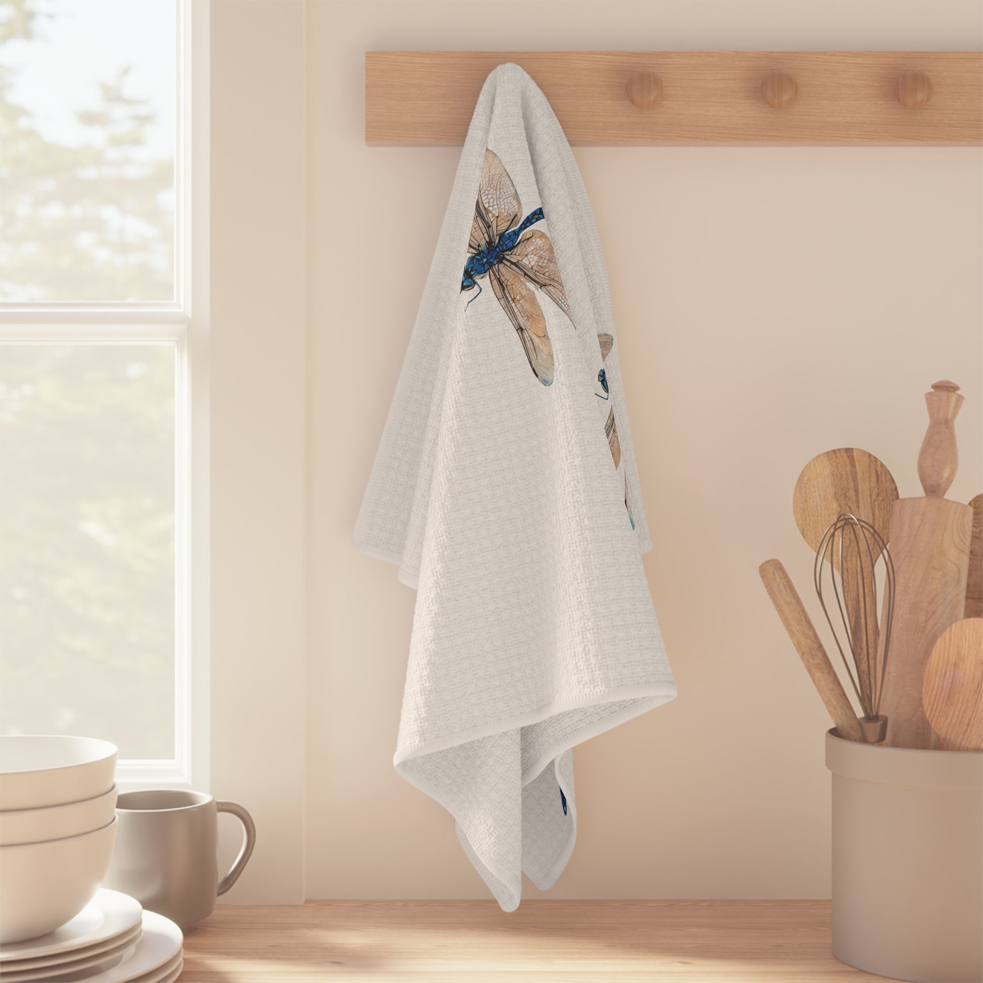 White towel with dragonfly design hanging on a wooden rack in a kitchen.