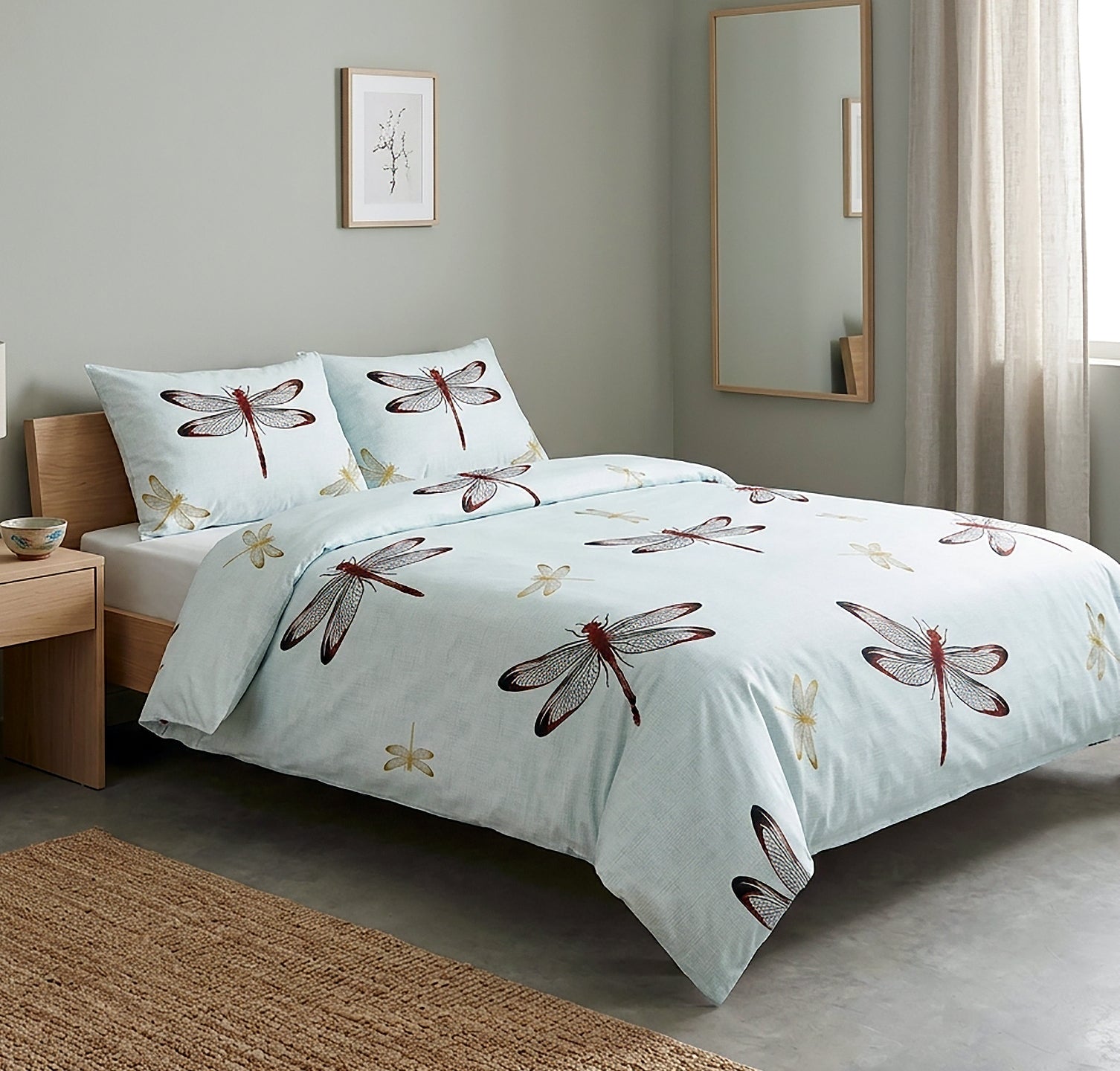 A light blue duvet cover and pillowcase set featuring a dragonfly print, styled on a wooden bed frame in a modern bedroom setting.