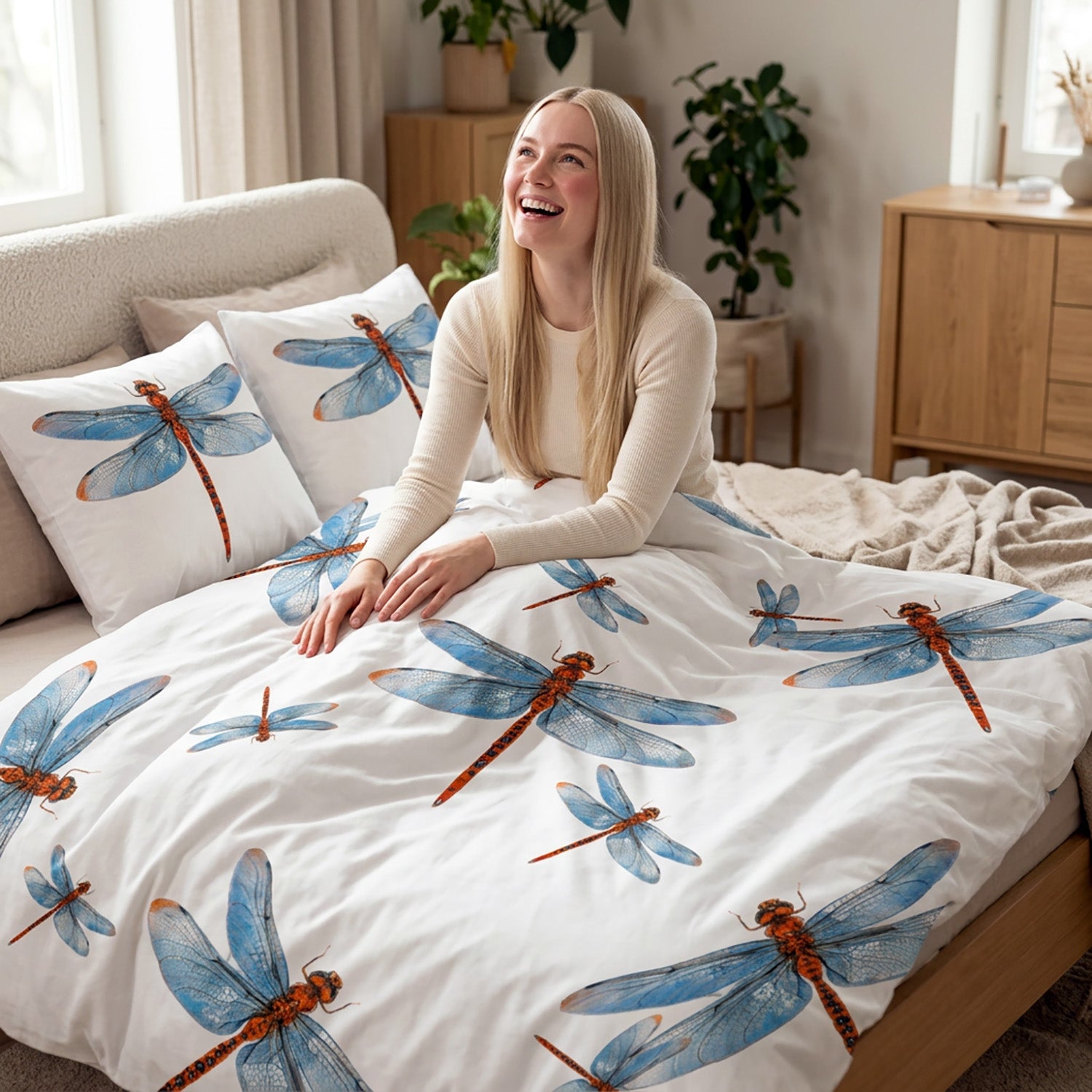 Woman sitting on a bed with dragonfly pattern bedding in a bright bedroom.