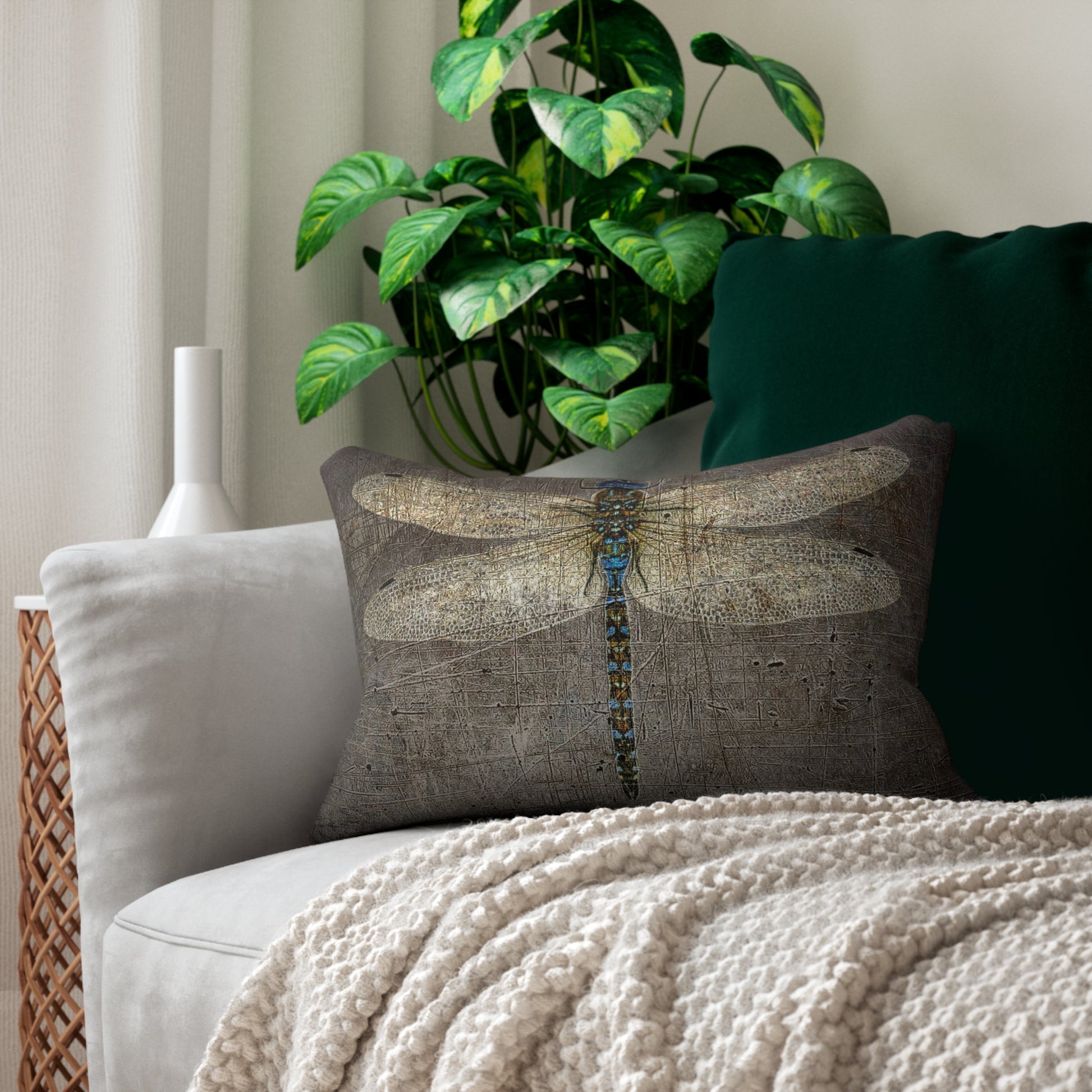 Decorative pillow with dragonfly design on a couch with a plant in the background