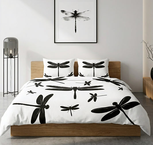 A bed dressed in a white duvet cover and matching pillowcases, printed with large black dragonfly silhouettes, shown in a modern bedroom setting with a wooden bed frame, wall art, and a floor lamp.