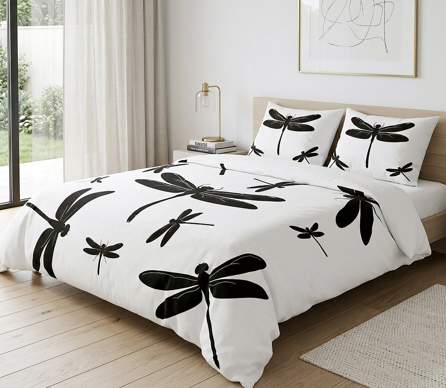 A bed dressed in a white duvet cover and matching pillowcases with large black dragonfly silhouettes, styled in a bright bedroom with wood flooring, a window, and a bedside lamp.