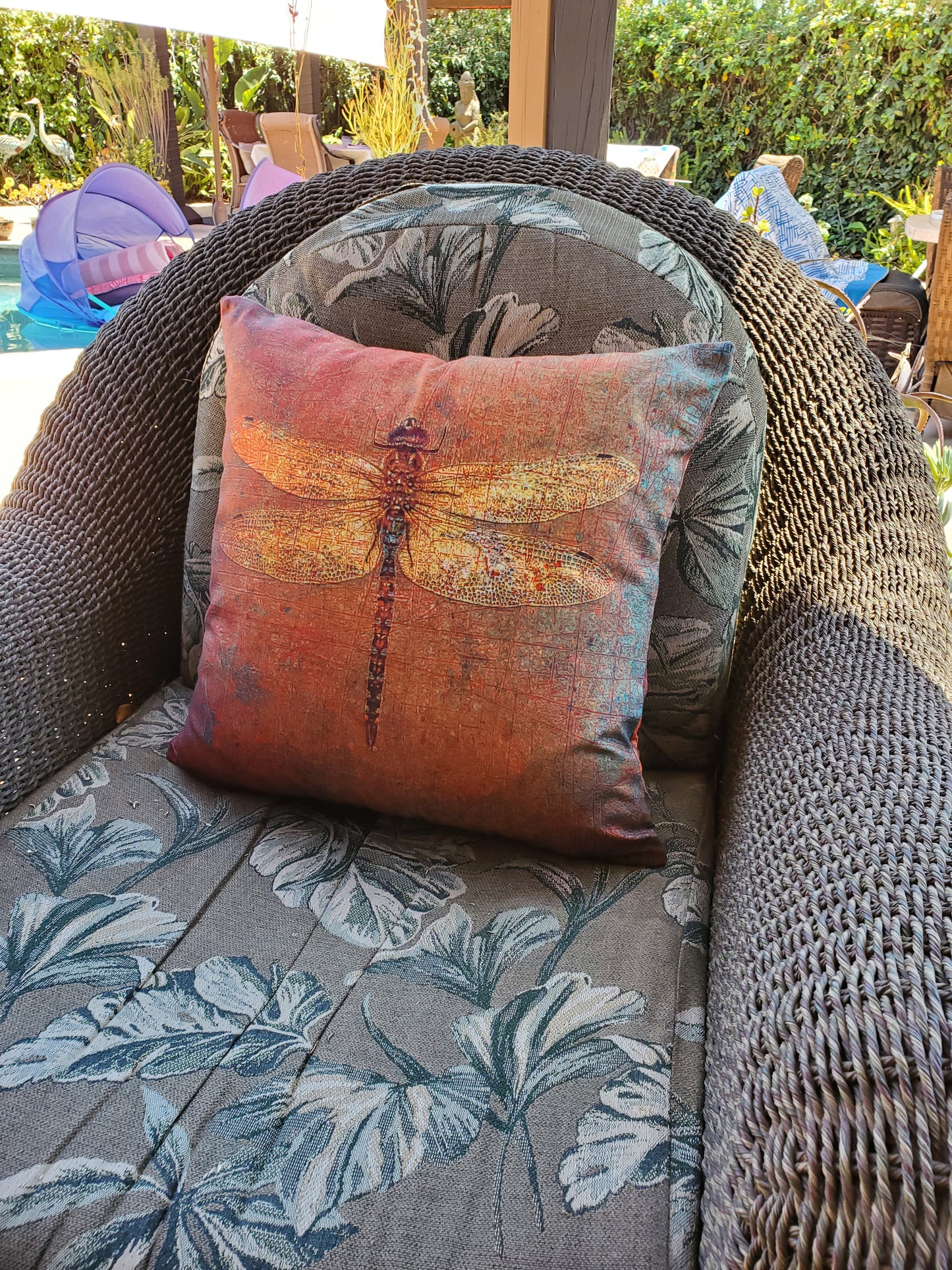 Decorative pillow with a dragonfly design on a wicker chair outdoors.