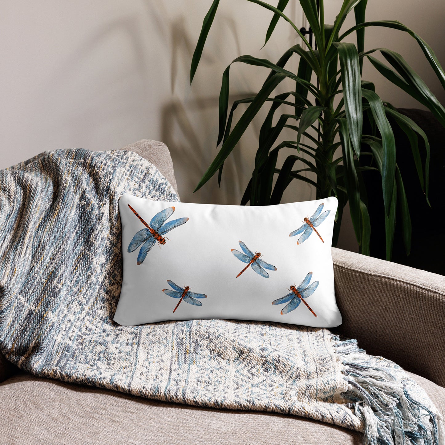 Decorative pillow with black and white pattern on a beige sofa with a textured blanket and plant in the background.