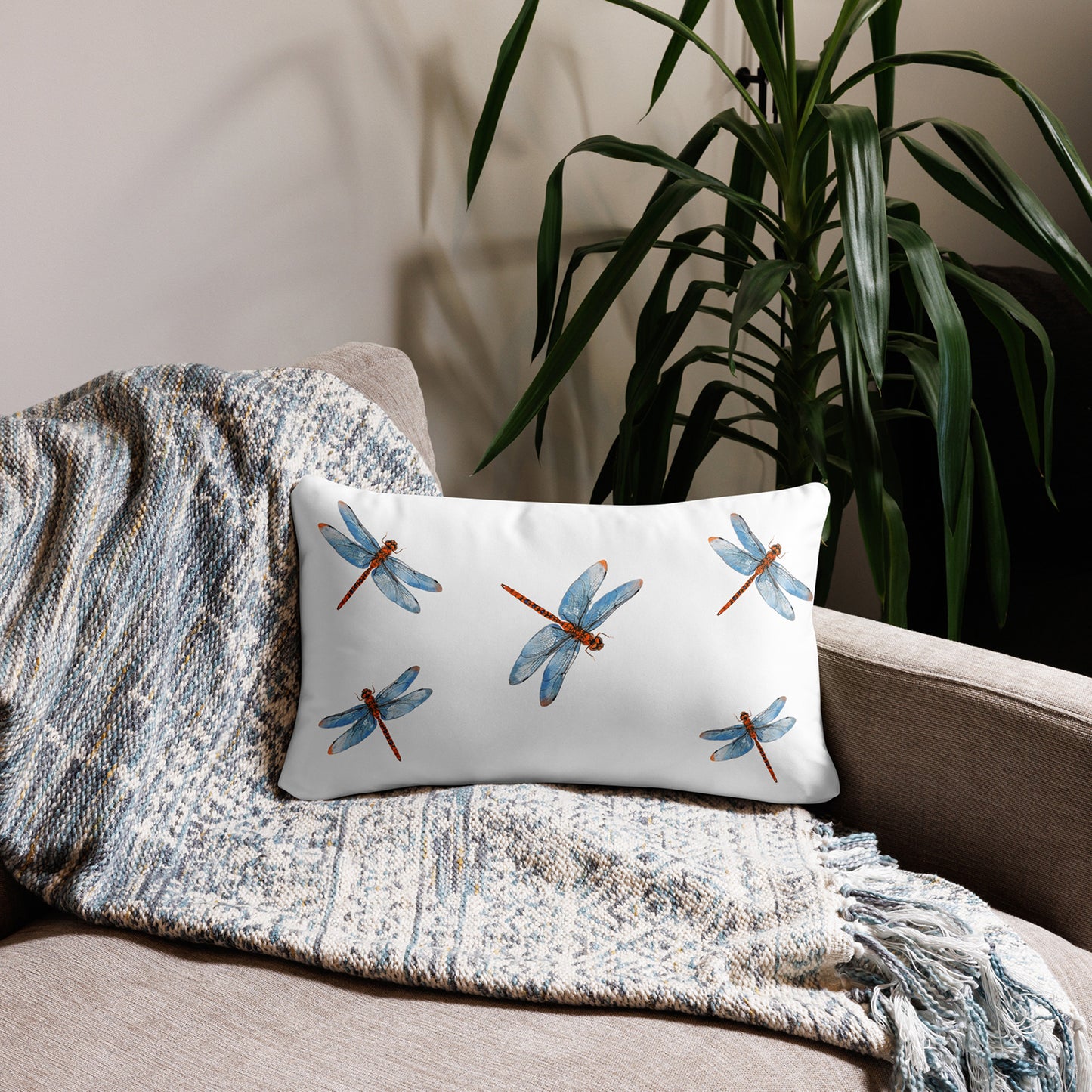 Decorative pillow with black and white pattern on a beige sofa with a textured blanket and plant in the background.