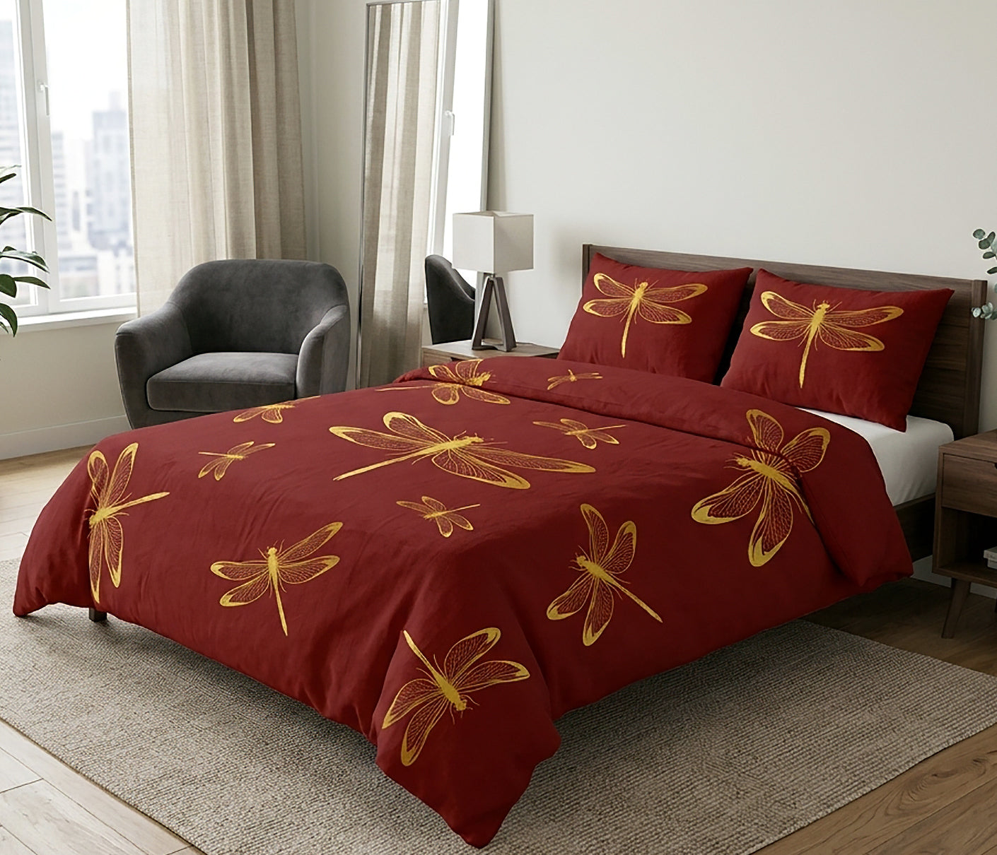 A bed dressed in a deep red duvet cover and matching pillowcases, both printed with large gold dragonfly motifs, shown in a styled bedroom setting with a gray armchair, window, and bedside lamp.