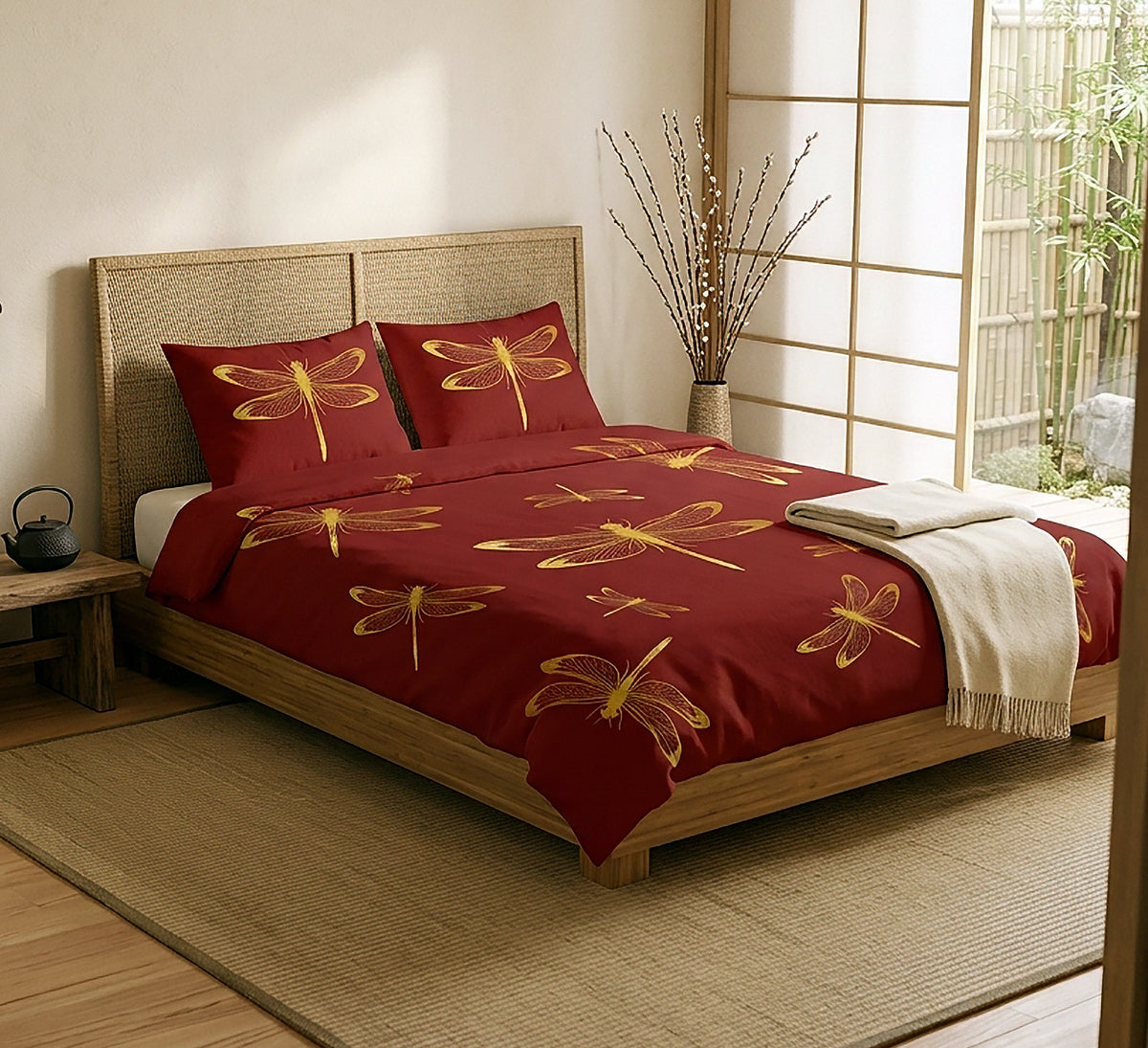 A bed dressed in a deep red bedding set with large gold dragonfly prints, styled in a Japanese-inspired bedroom with a wooden headboard, shoji screen, and a folded cream throw blanket.