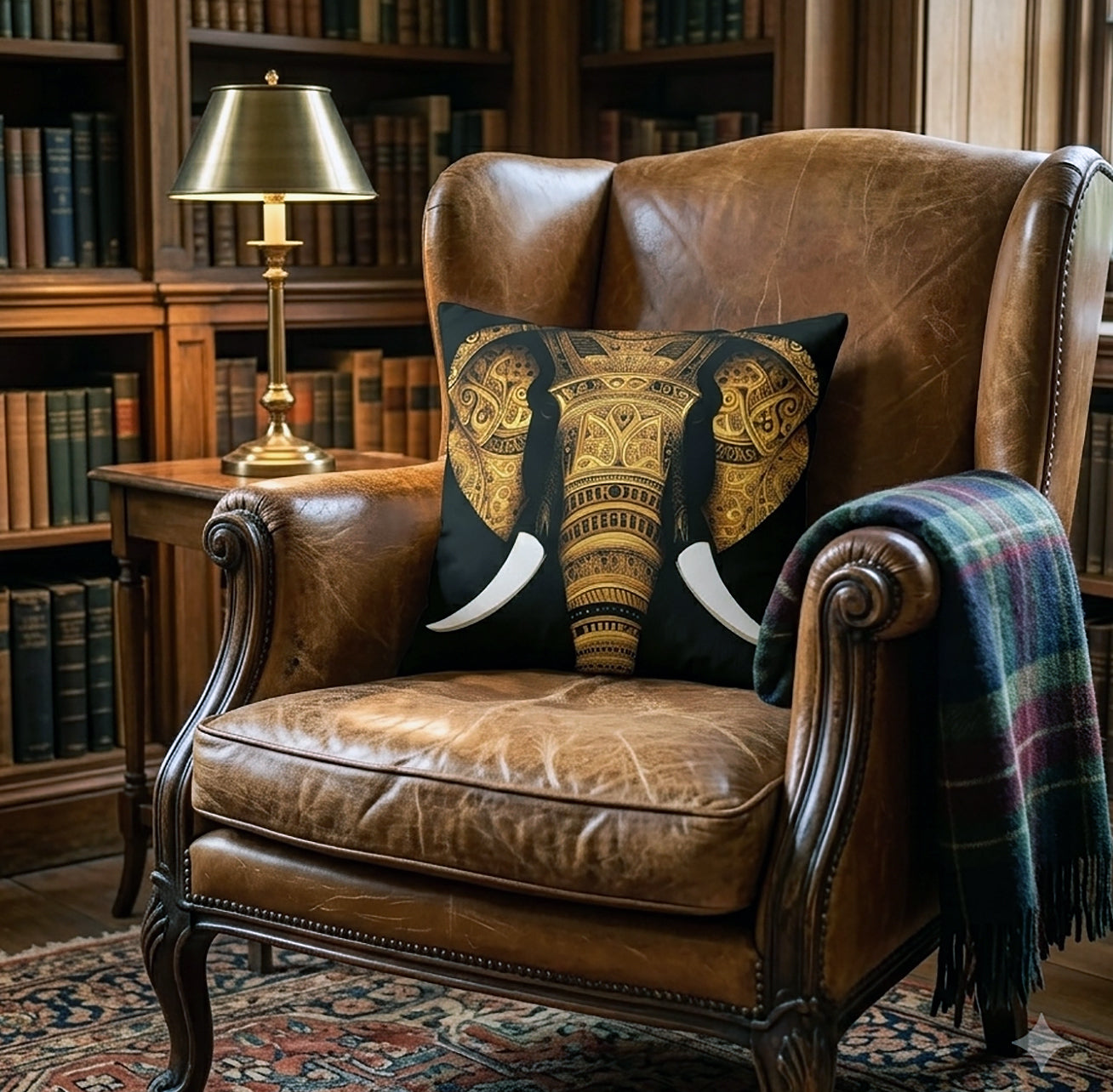 A brown leather armchair in a library setting with a decorative elephant-print throw pillow and a plaid throw blanket.