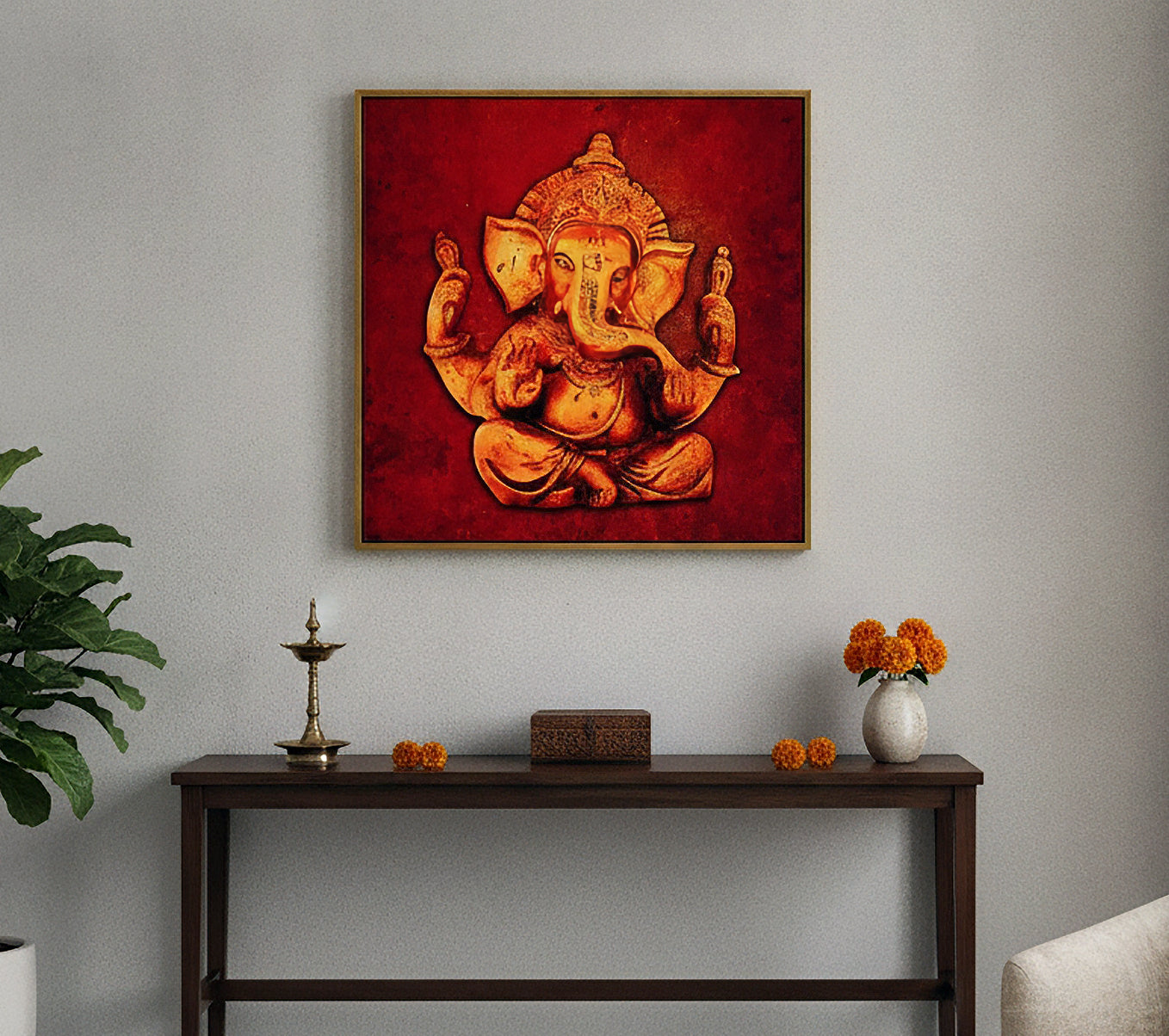 A framed square wall art print depicting a golden Ganesha on a textured red background, hanging on a light gray wall above a dark wooden console table with decorative items.