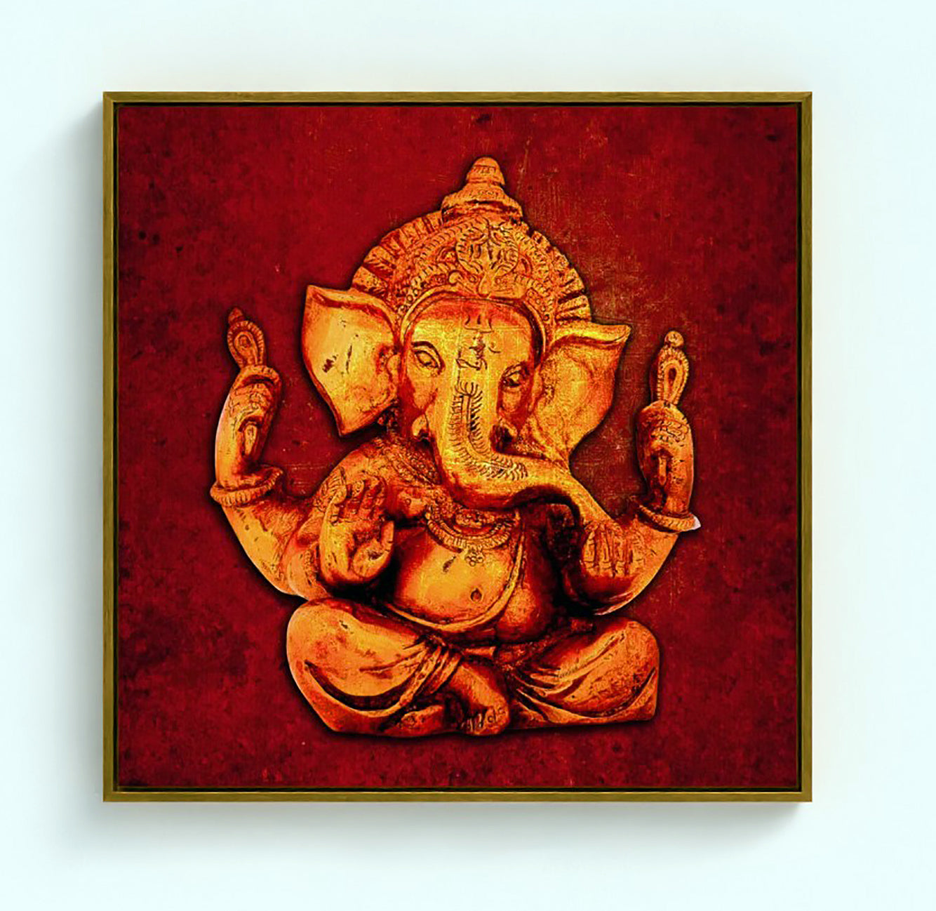 A square framed wall art print featuring a golden-toned seated Ganesha figure on a textured deep red background, shown against a light gray wall.