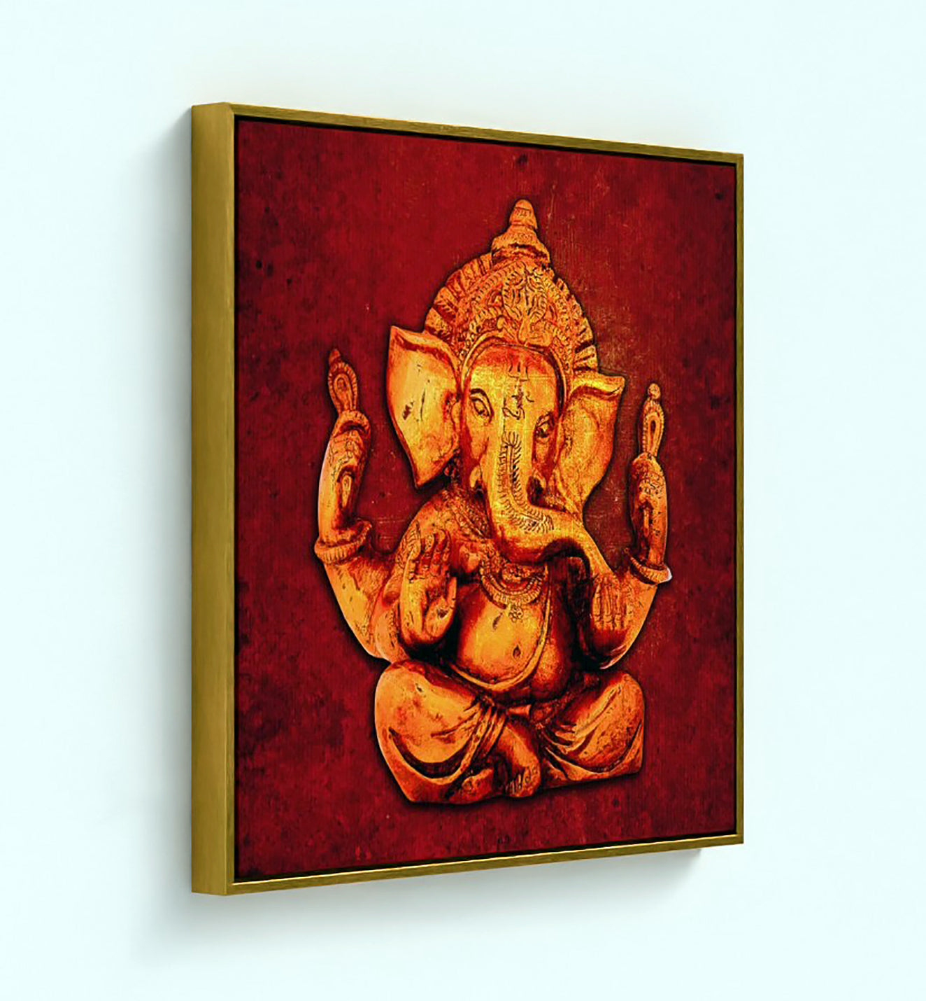 A framed wall art print featuring a golden Ganesha figure on a textured deep red background, shown hanging against a light blue wall.