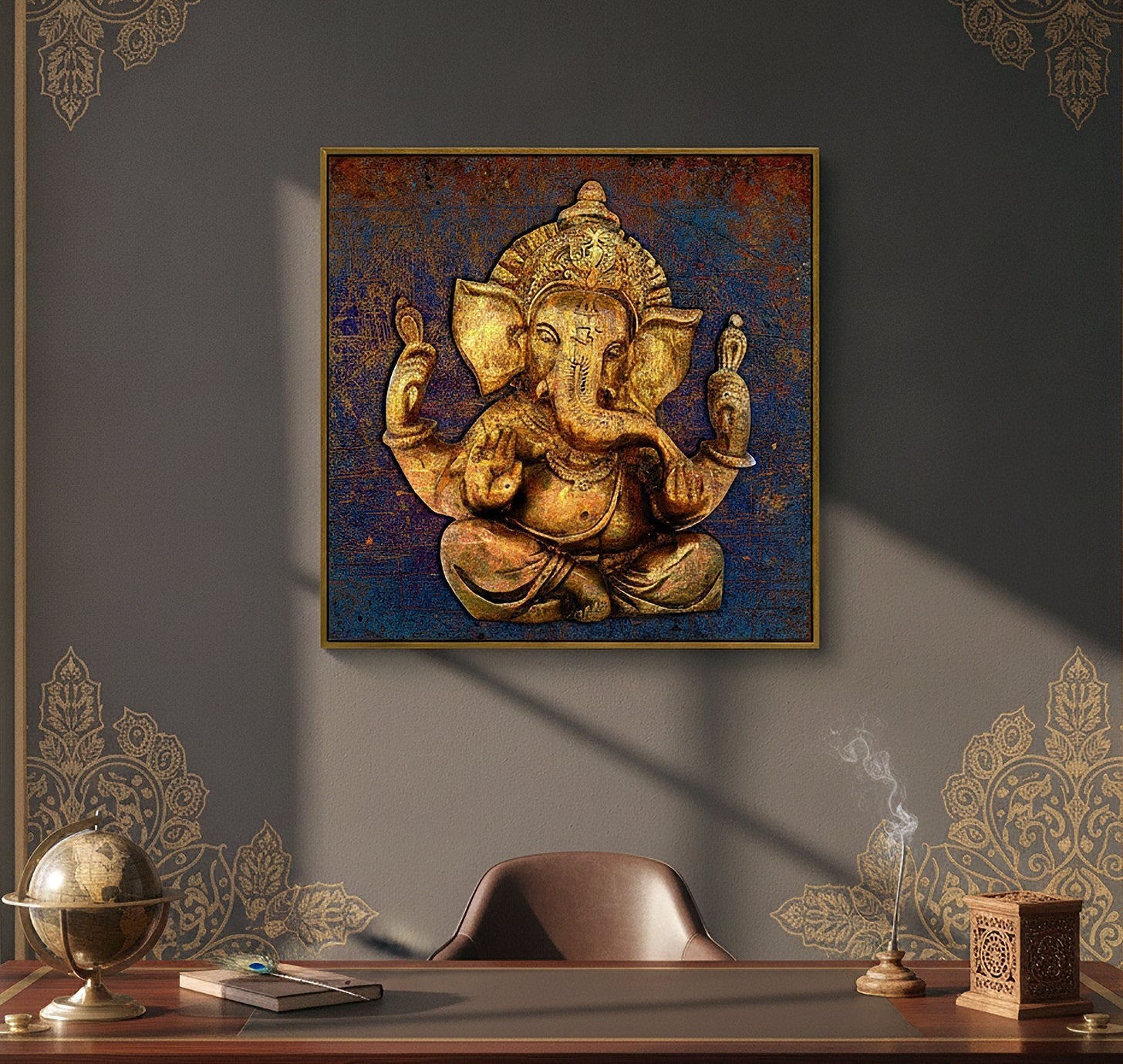 A square framed wall art print depicting a golden Ganesha figure against a textured blue and brown background, displayed on a dark gray wall above a wooden desk with decorative objects.