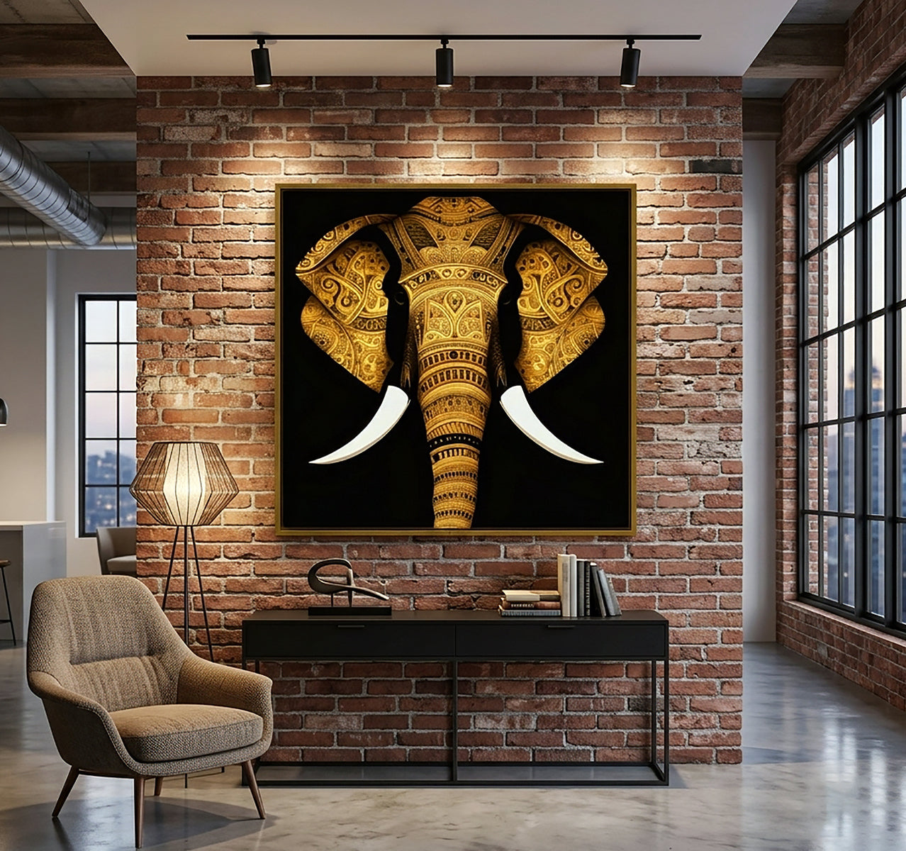 A large framed wall art print of an ornate golden elephant head with white tusks, displayed on a brick wall above a console table in a modern loft-style room with a chair, lamp, and large windows.