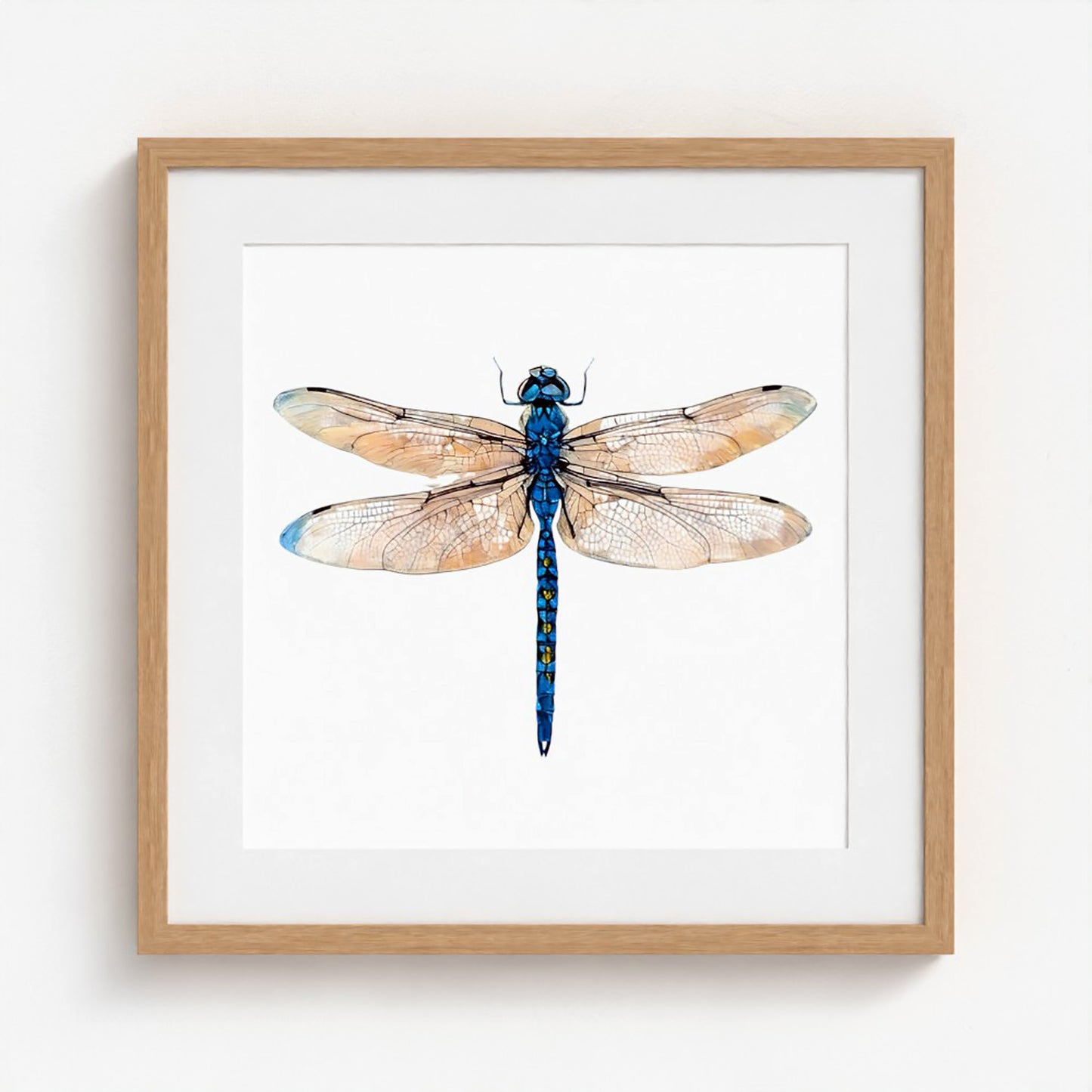 Framed wall art featuring a watercolor-style dragonfly centered on a white mat, set in a light natural wood frame against a white wall.