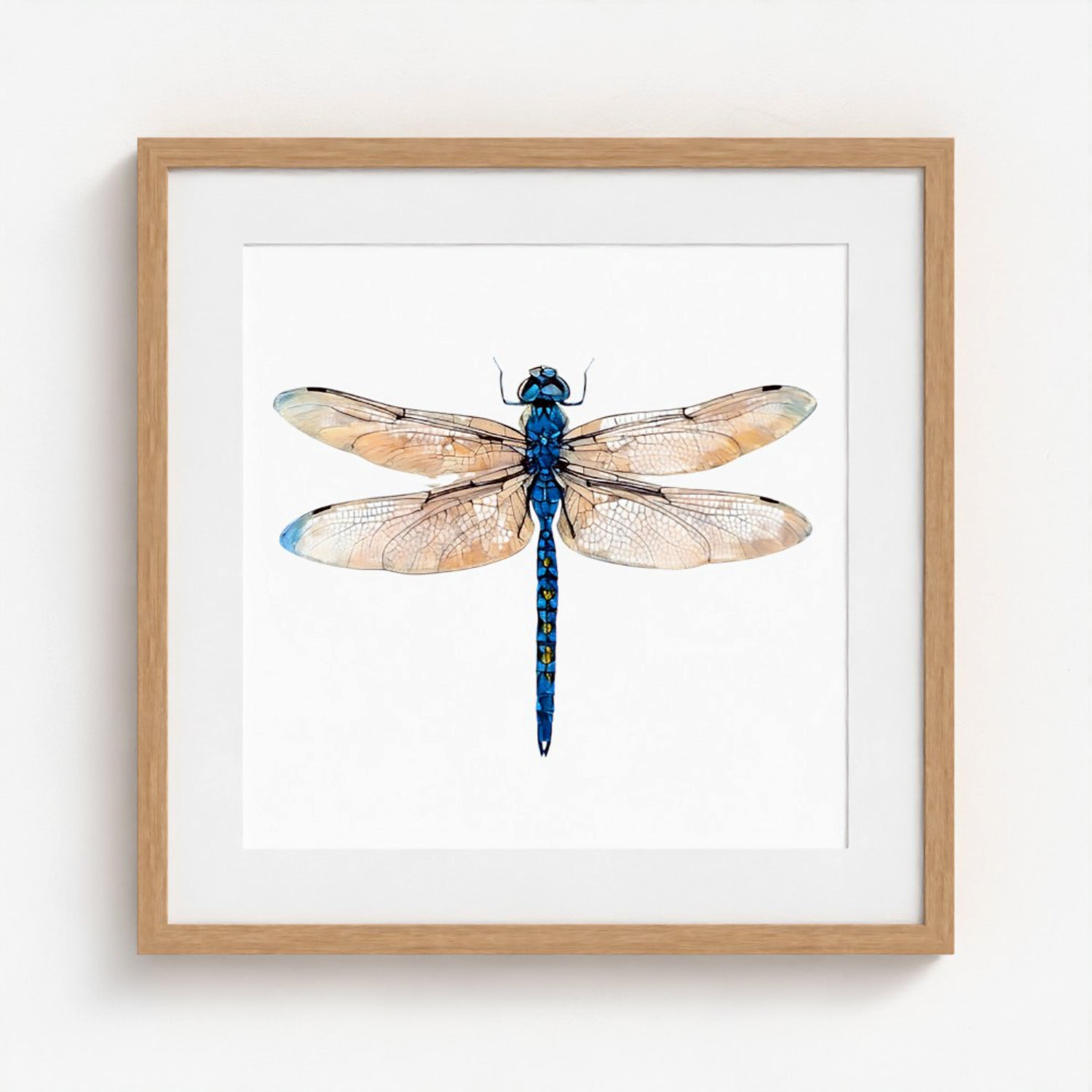 Framed wall art featuring a watercolor-style dragonfly centered on a white mat, set in a light natural wood frame against a white wall.
