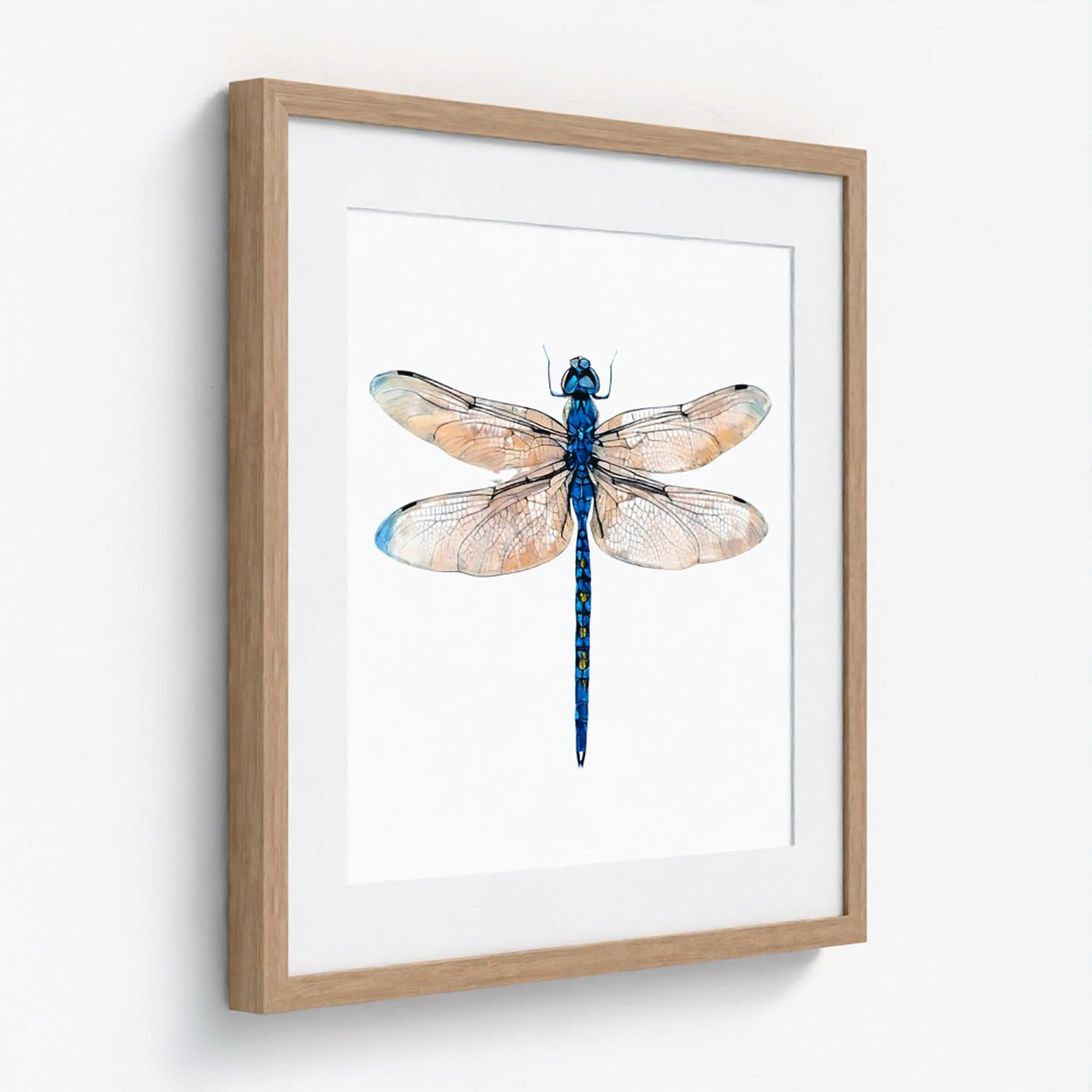 Framed wall art featuring a watercolor-style blue dragonfly centered on a white mat, set in a light natural wood frame against a white wall.