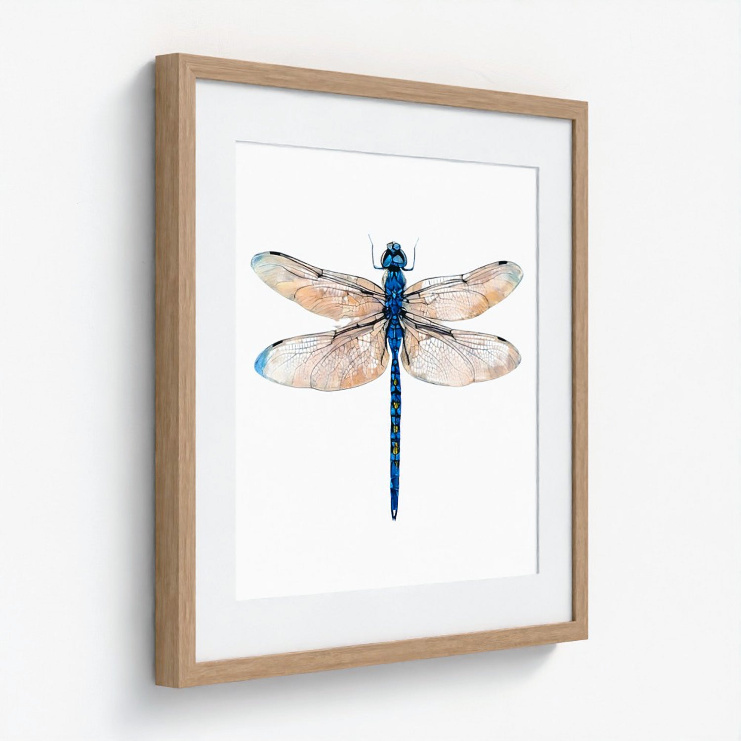 Framed wall art featuring a watercolor-style blue dragonfly centered on a white mat, set in a light natural wood frame against a white wall.