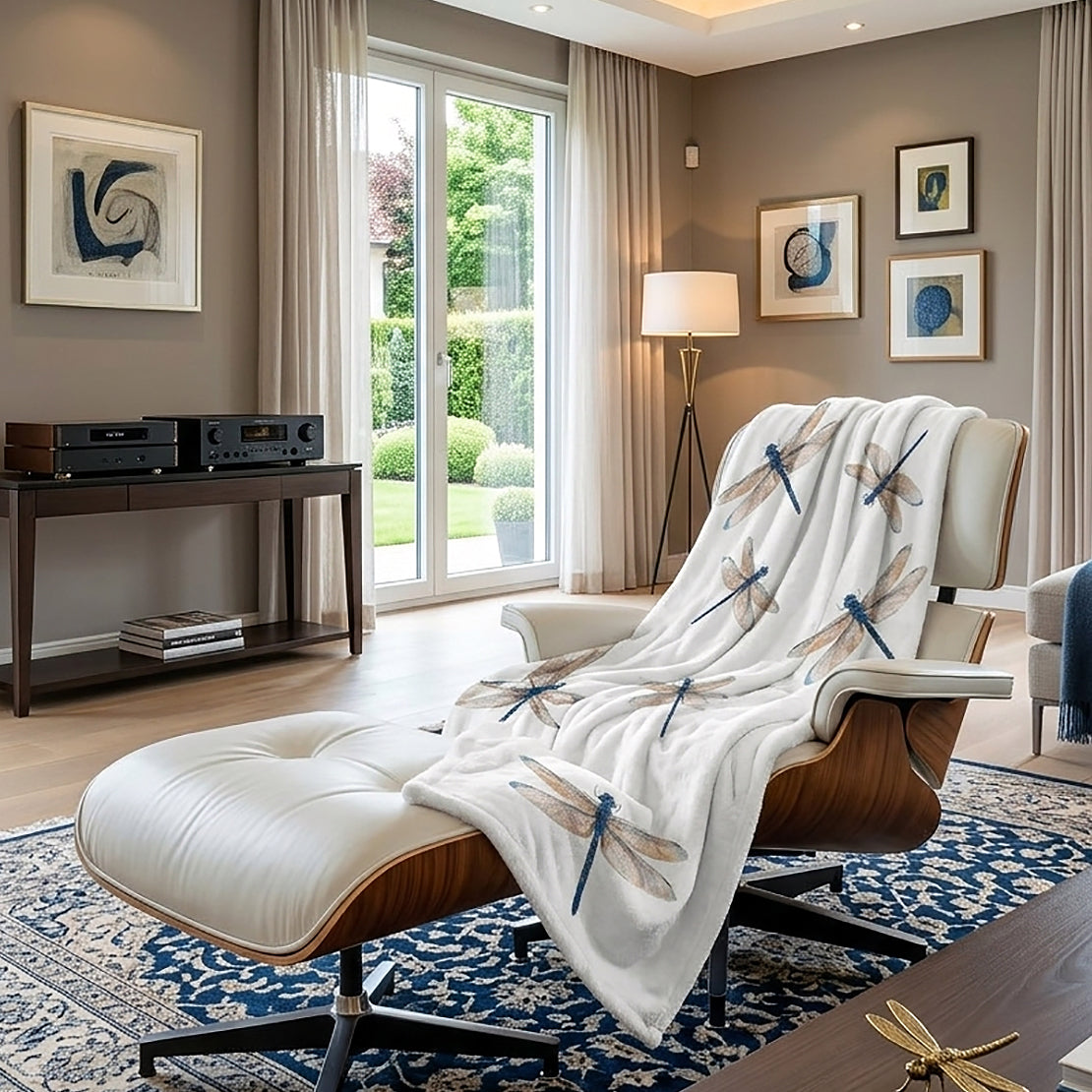 A white throw blanket with a blue and brown dragonfly pattern is draped over a mid-century modern lounge chair in a stylishly decorated living room.
