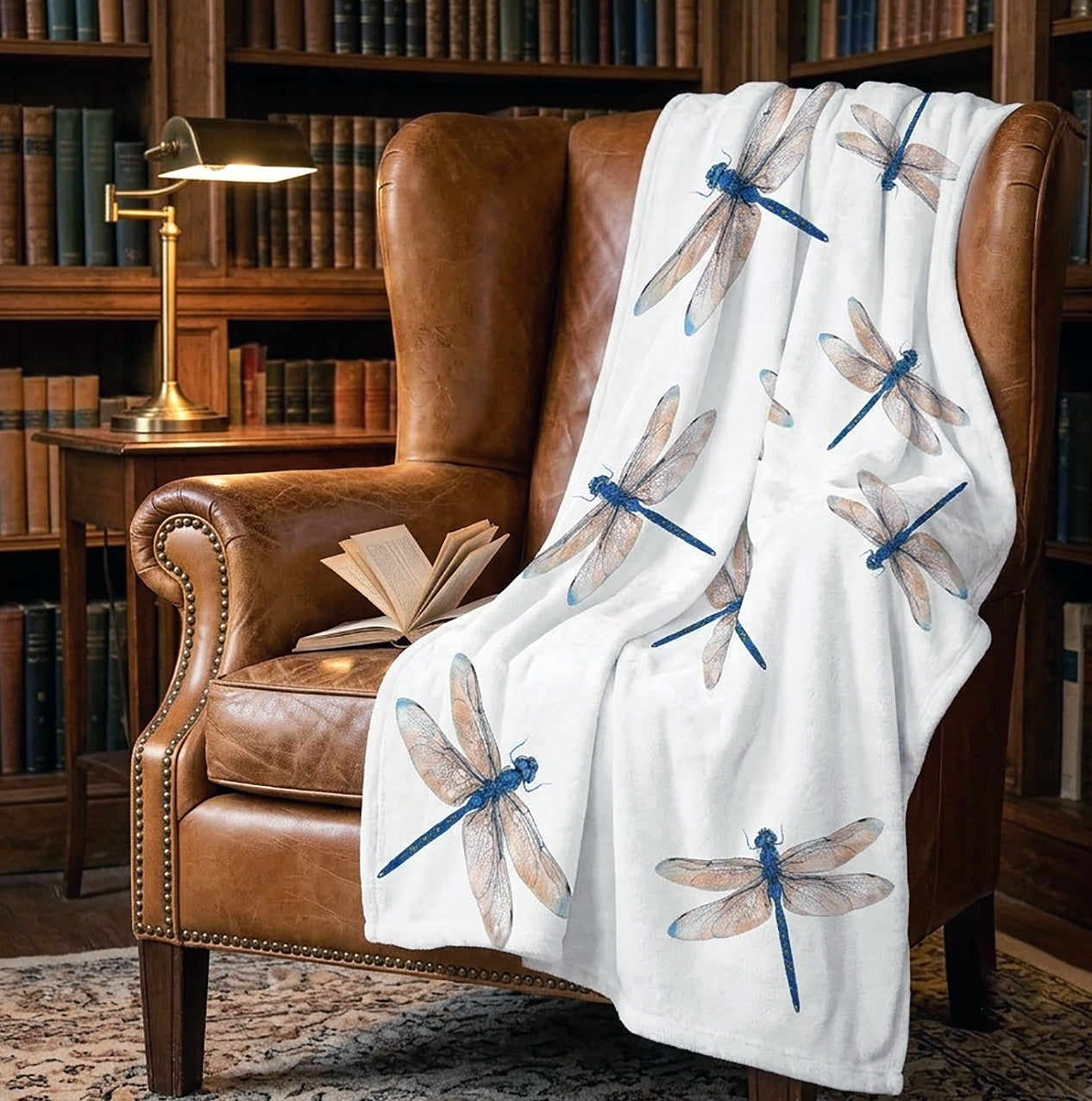 A white throw blanket draped over a brown leather armchair in a cozy library setting, featuring a pattern of blue and beige dragonflies.