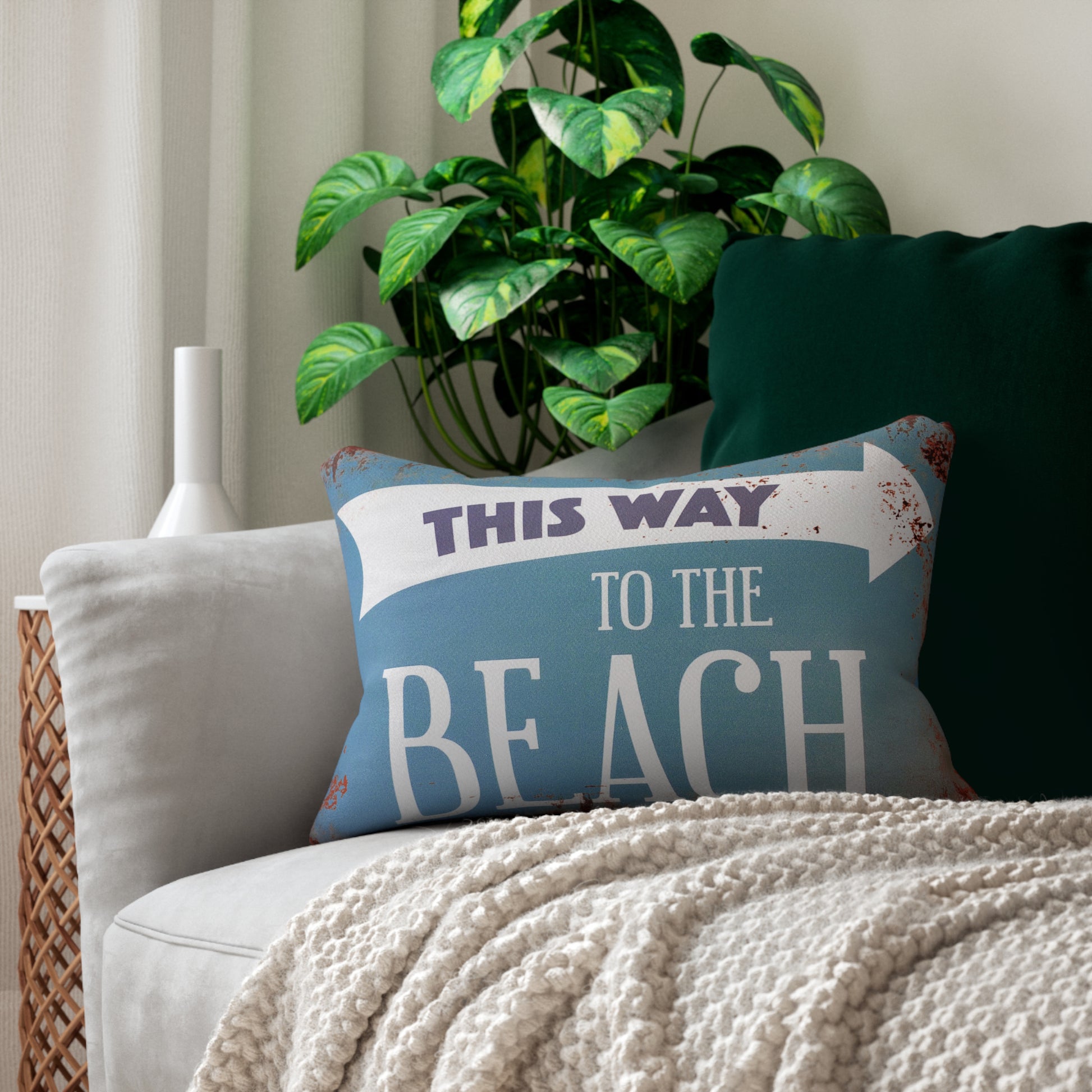 Decorative pillow with 'This Way to the Beach' text on a couch with a plant in the background